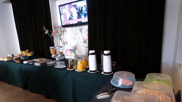 Une table de buffet garnie de divers plats et boissons, un écran de télévision en arrière-plan et une composition florale décorative.