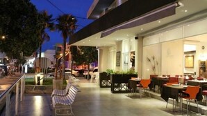 Un espace extérieur aménagé pour les repas, avec des tables et des chaises, un banc et un chemin menant à l’entrée.