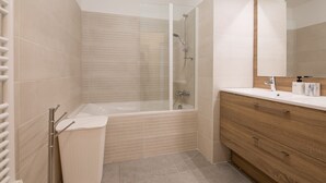Un baño moderno con cabina de ducha de vidrio, tocador de madera con espejo y lavamanos blanco.