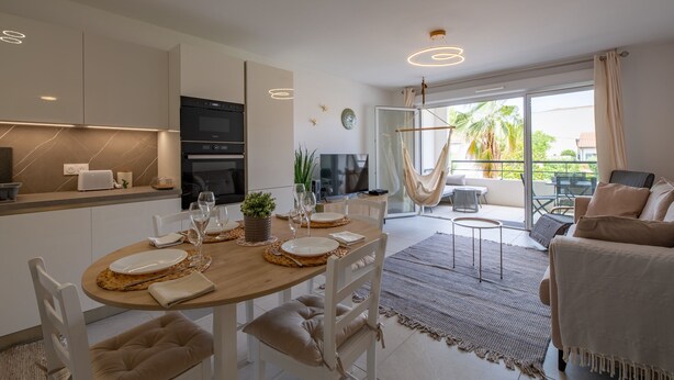 Una cocina moderna con electrodomésticos integrados, una zona de comedor con una mesa redonda y un balcón con vistas a palmeras.