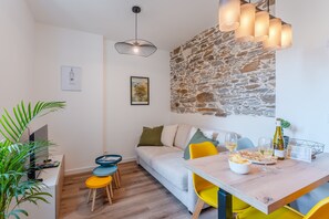 A modern living room with a stone accent wall, a dining area with a wooden table and yellow chairs, and a cozy seating area with a sofa and cushions. - Gustave - Proche centre-ville de Nantes (Nantes)