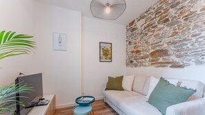 A modern living room with a stone wall, a white sofa with green and white cushions, a small blue and yellow table, and a TV on a white stand. - Gustave - Proche centre-ville de Nantes (Nantes)