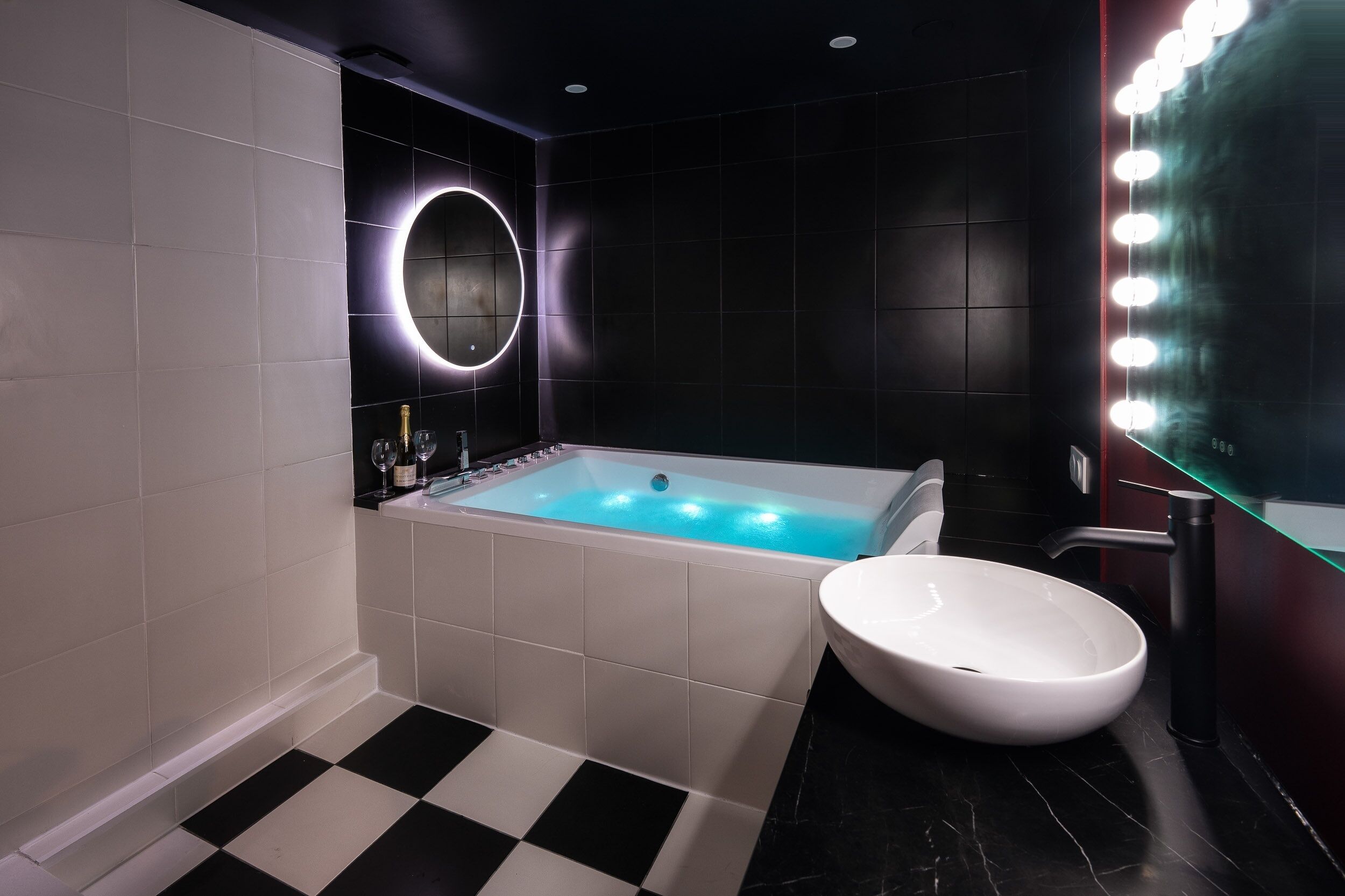 Une salle de bain moderne avec une grande baignoire, un grand miroir rond doté de lumières et un lavabo blanc.