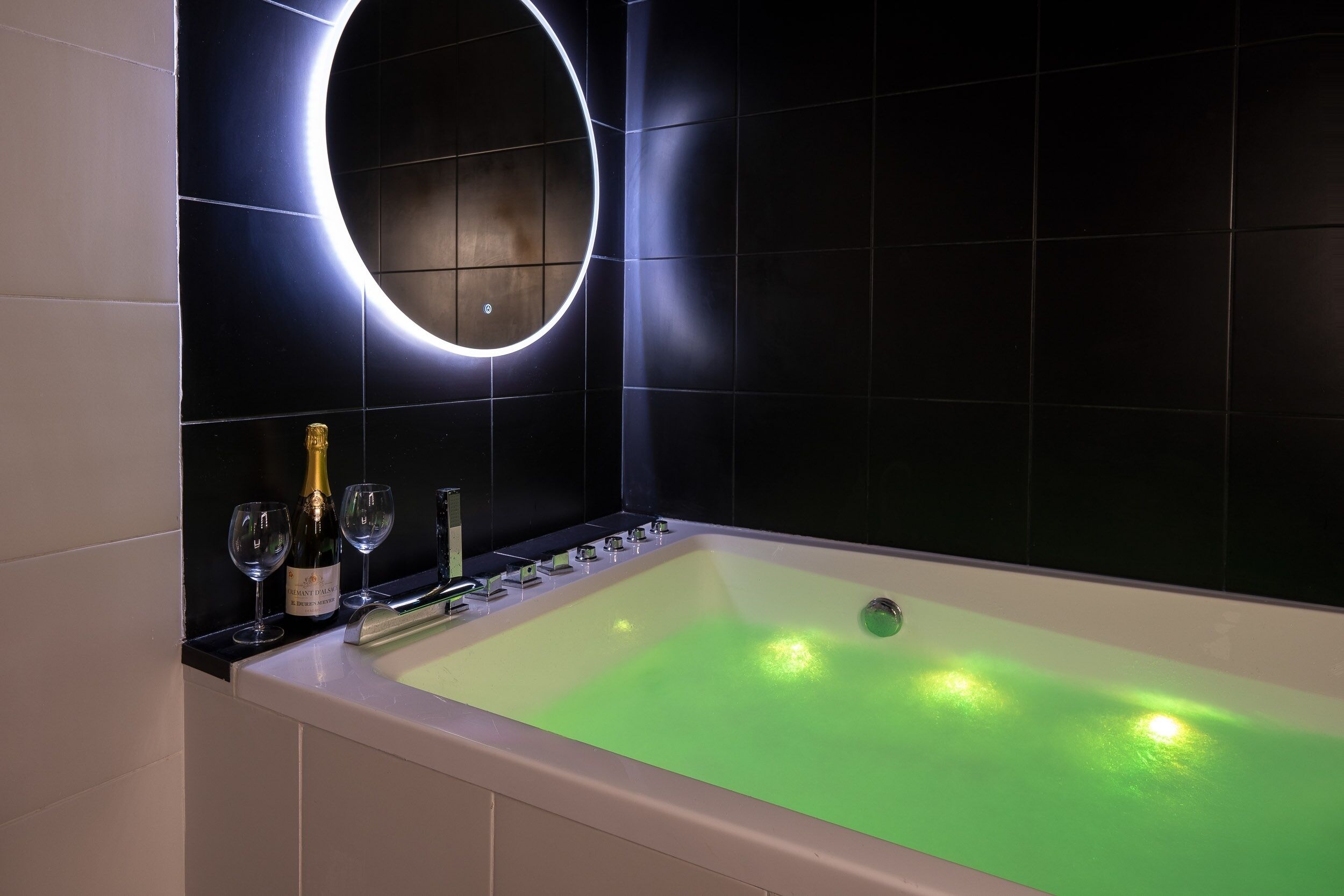 Un baño moderno con una bañera grande, un espejo circular y una botella de champán.