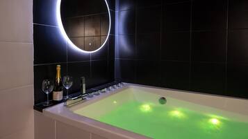 Un baño moderno con una bañera grande, un espejo circular y una botella de champán.