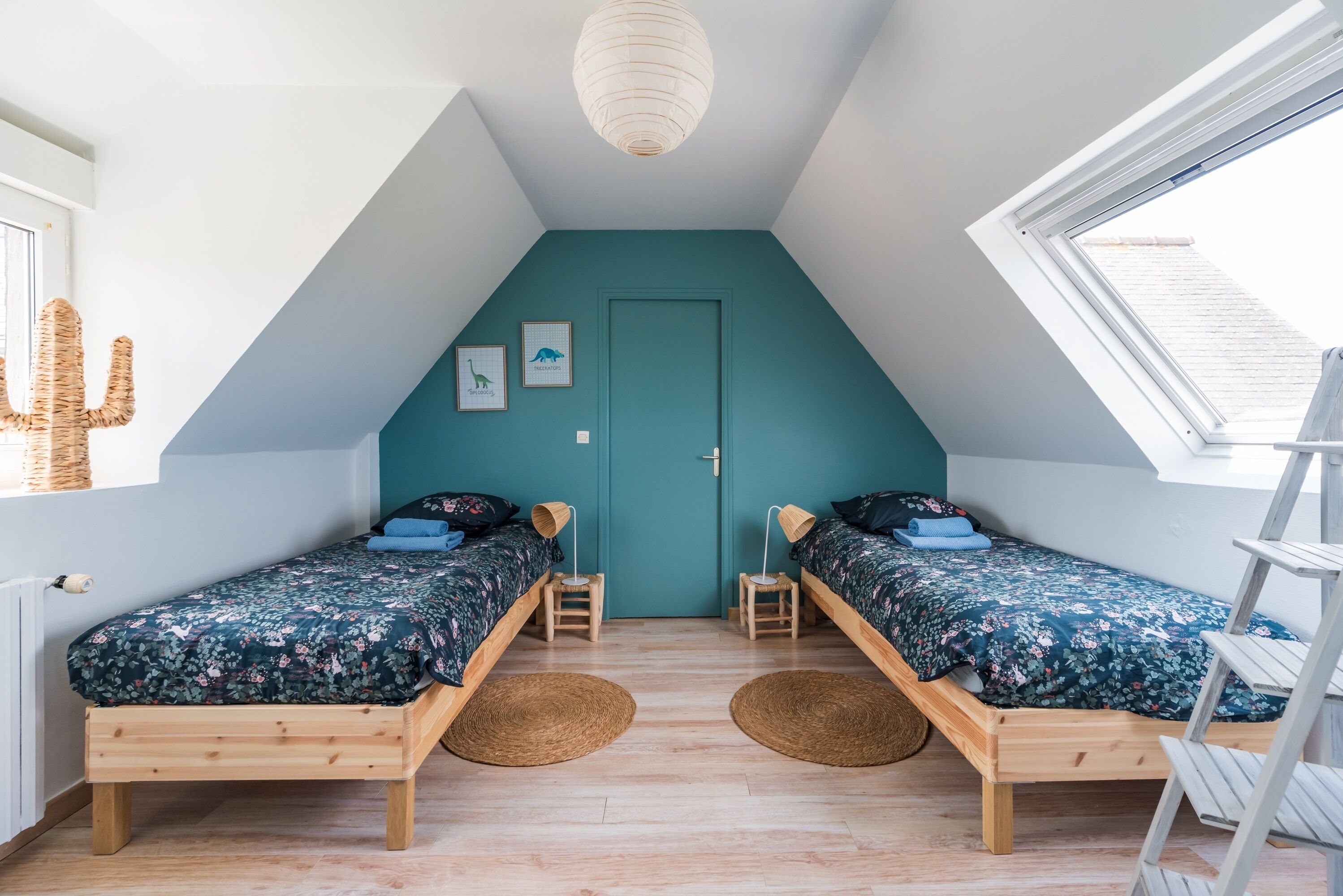 Een kamer met twee houten bedden, een muur in teal, een dakraam en een ladder.