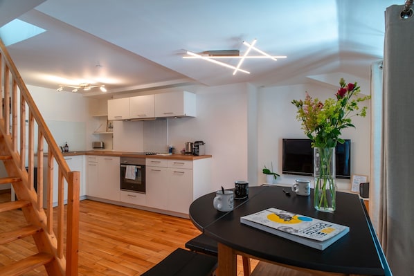 A modern kitchen with white cabinets, a wooden staircase, and a dining area with a table and chairs.