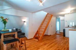 A modern kitchen with wooden flooring, a staircase, and a dining area with a table and chairs.