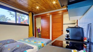 A room with a bed, a small kitchenette, and a sliding door closet. - Studio Pitaya - Vue mer et piscine partagée (Les Avirons)