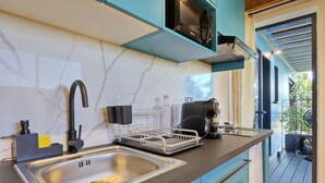 A modern kitchen with a stainless steel sink, a black faucet, a microwave, and a coffee maker on the countertop. - Studio Pitaya - Vue mer et piscine partagée (Les Avirons)