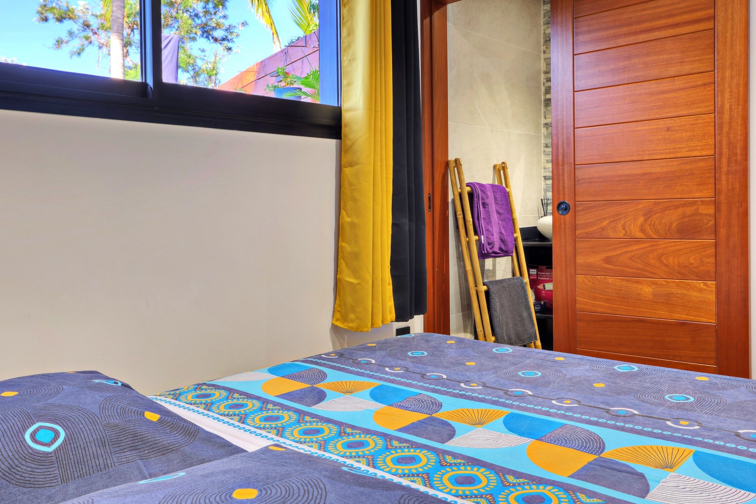 Een kamer met een bed, een houten garderobe, een raam met gordijnen en uitzicht op het omliggende landschap.