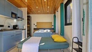 A compact bedroom with a bed, bedside table, and a window with curtains. - Studio Ananas - Vue mer et piscine partagée (Les Avirons)