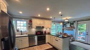 A modern kitchen with white cabinets, stainless steel appliances, and a large island. - Maine Coast Mountain Retreat (Camden)
