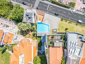 Luchtbeeld van een modern hotel met een zwembad op het dak, meerdere gebouwen en een straat met auto's.