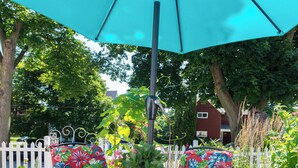 Ein runder Tisch mit einer blumigen Tischdecke, umgeben von Stühlen mit tropischen Mustern, unter einem großen Sonnenschirm.