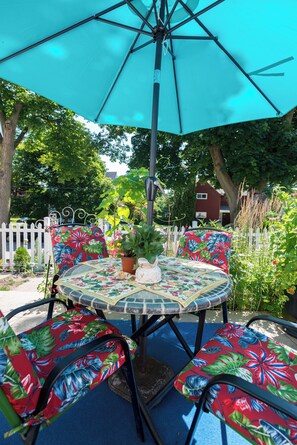 Een ronde tafel met een tafelkleed met bloemenprint, omringd door stoelen met tropische motieven, onder een grote parasol.