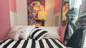 Ein Bett mit schwarz-weiß gestreifter Bettwäsche, ein rosa Kissen mit Text und ein farbenfrohes Bild an der Wand.