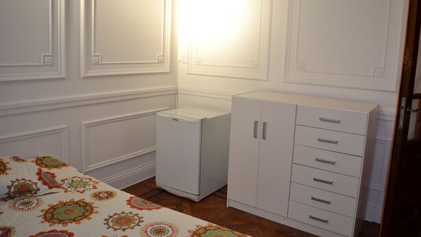 Una habitación con una cama, un armario pequeño blanco y un zócalo decorativo en la pared.