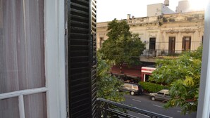 Un balcón con vista a una calle, un edificio con toldo rojo y un árbol.