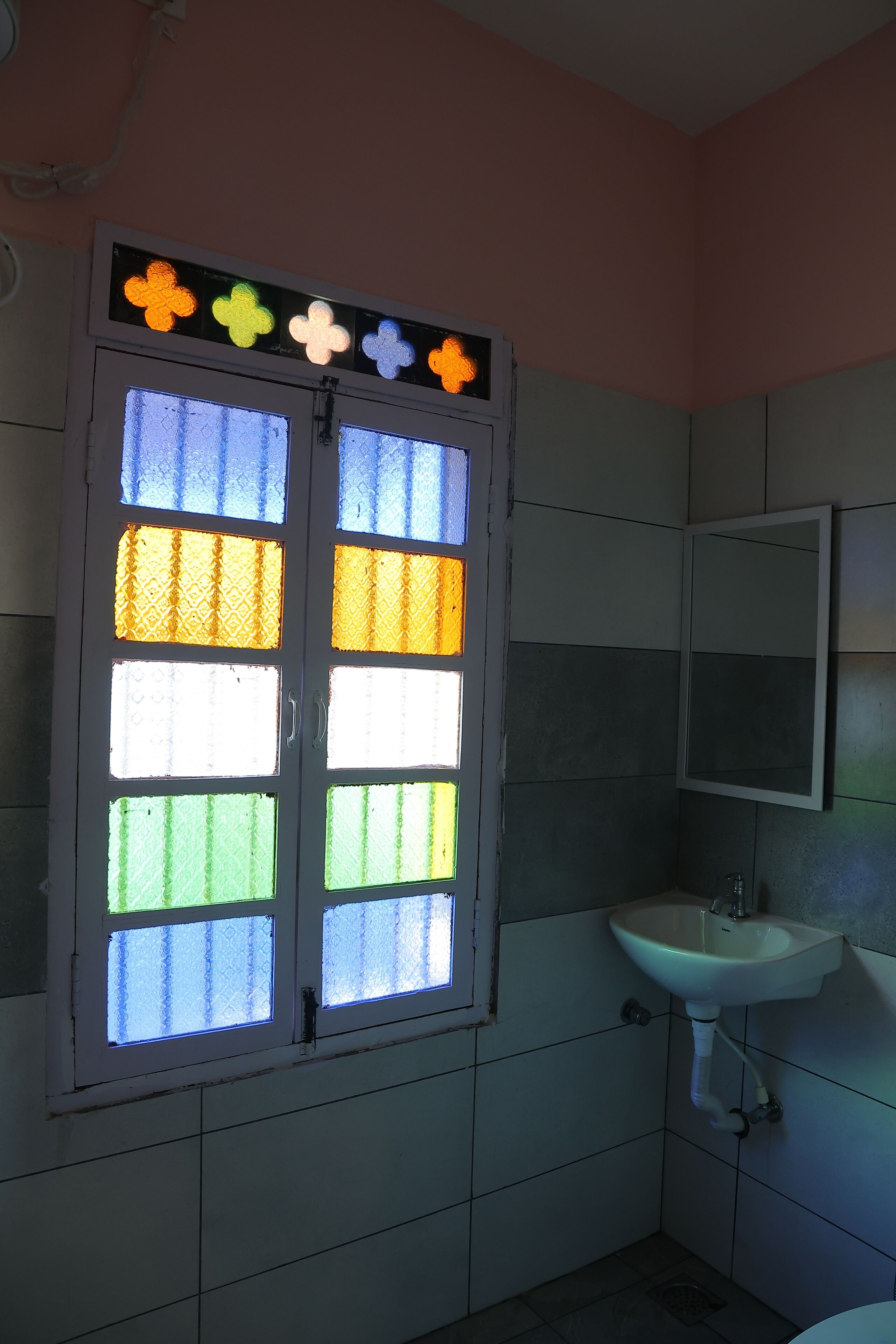 Une salle de bain avec une fenêtre ornée de vitraux, un lavabo et un miroir.