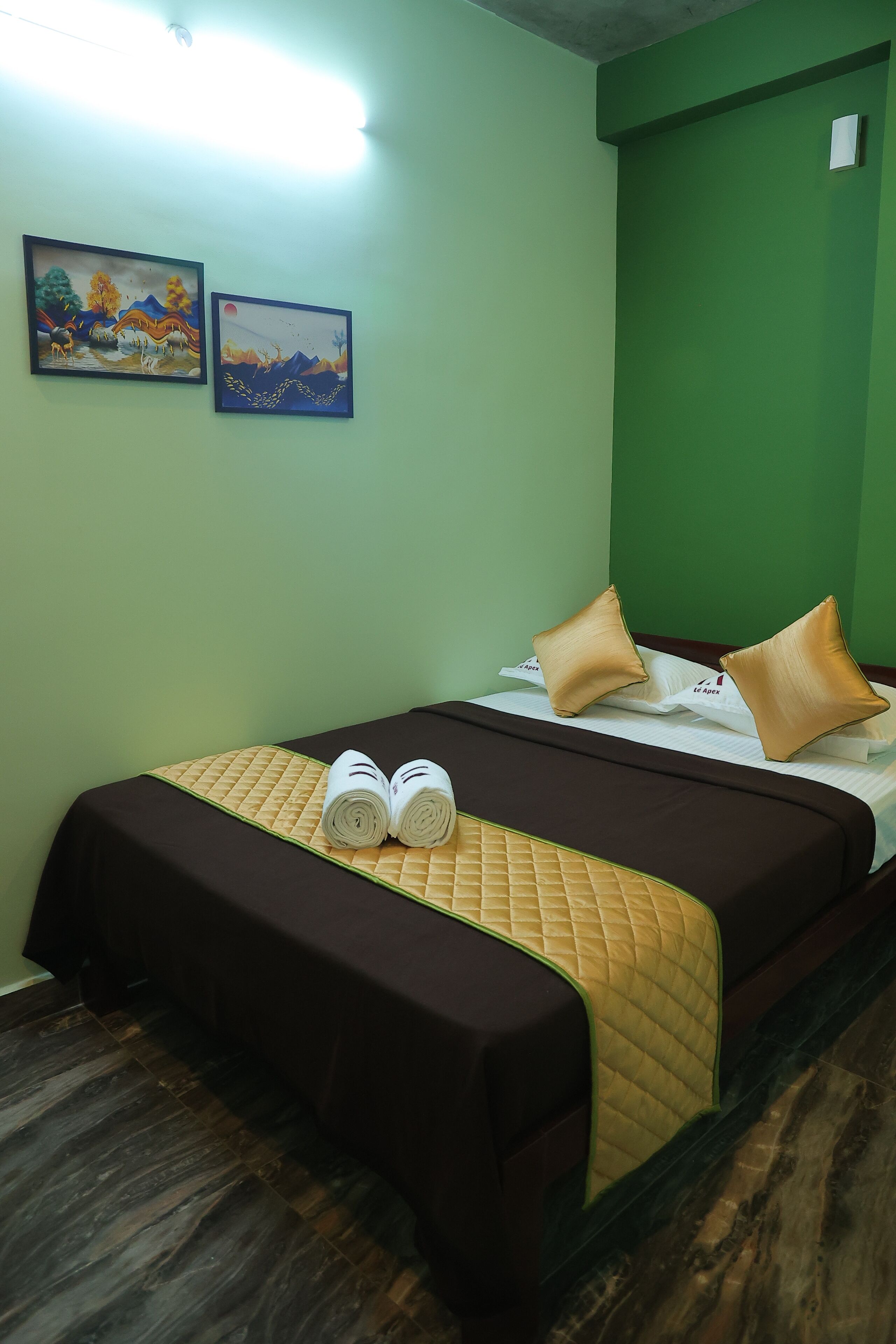 A hotel room with a bed, pillows, a quilted bedspread, and two paintings on the wall.