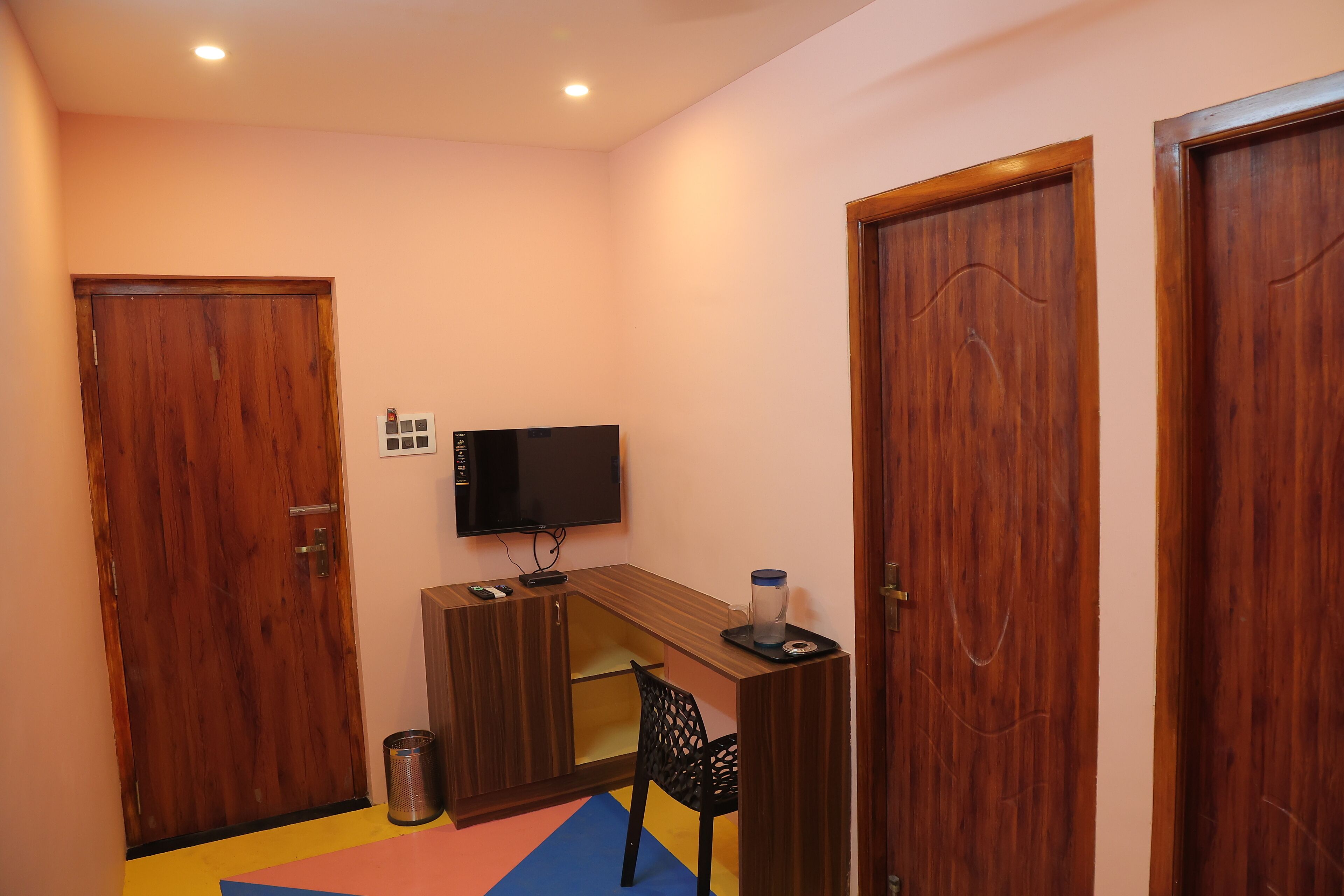 Ein kleines Zimmer mit einem Holztisch, einem Fernseher, einem Mülleimer und einem farbenfrohen Teppich.