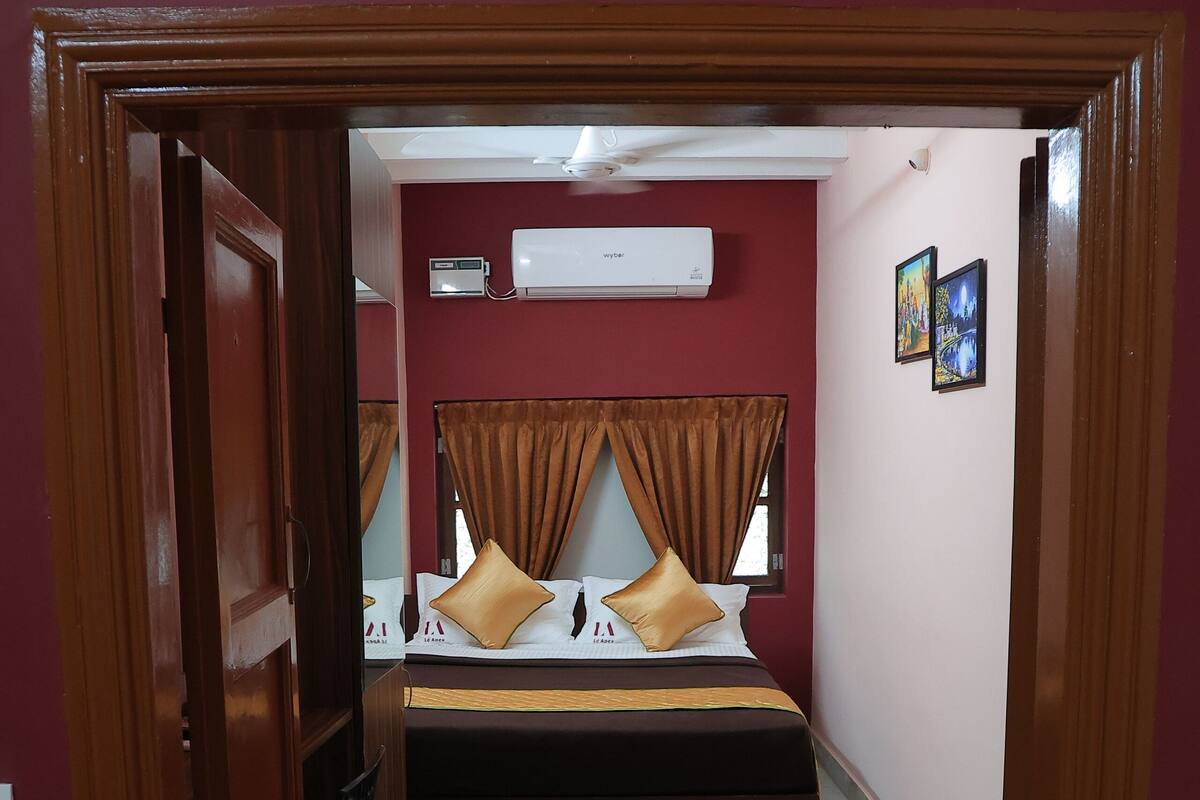 A bedroom with a bed, two pillows, a bedside table, and a wall-mounted air conditioner.