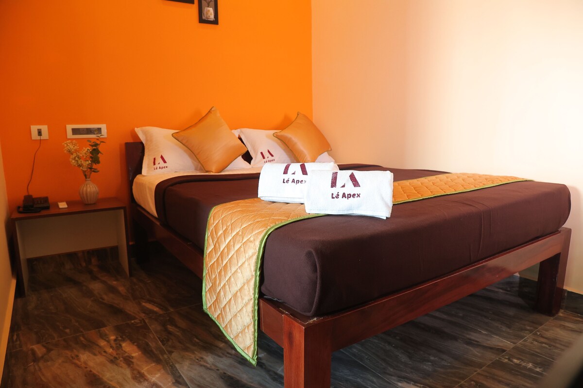 A hotel room with a bed, pillows, a nightstand, a vase with flowers, and a wall with a picture.