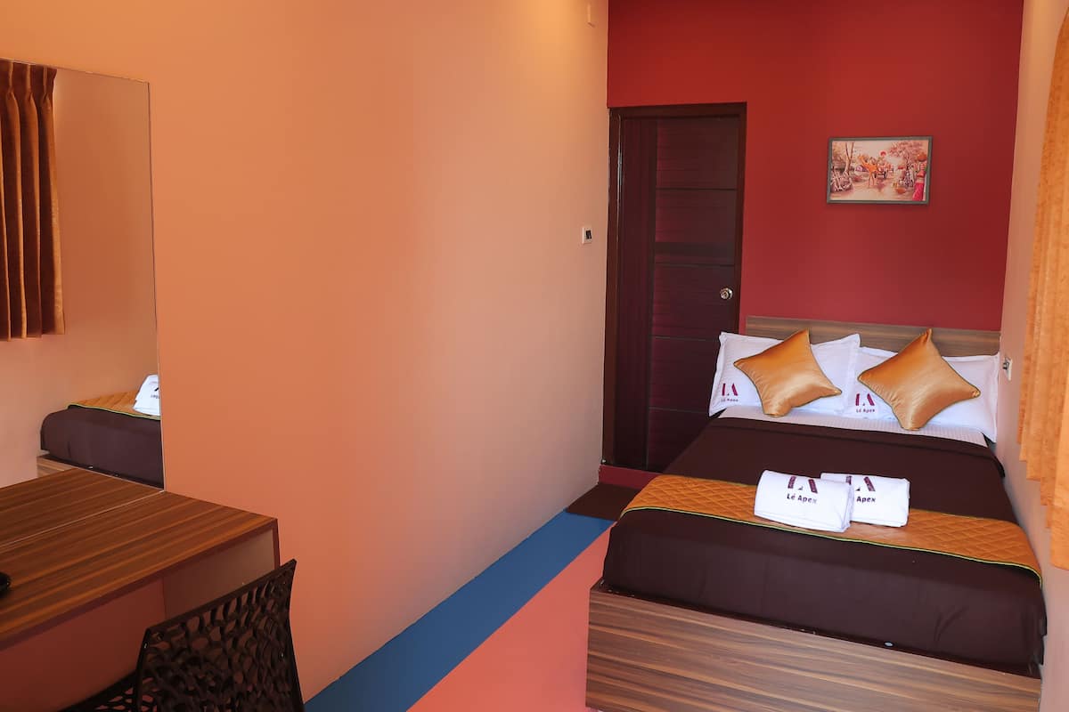 A hotel room with a bed, a desk, a chair, a mirror, and a door.