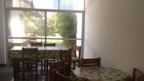 A dining area with a large window, wooden tables with floral tablecloths, and chairs. - Pindo Guazu Hostel (Buenos Aires)