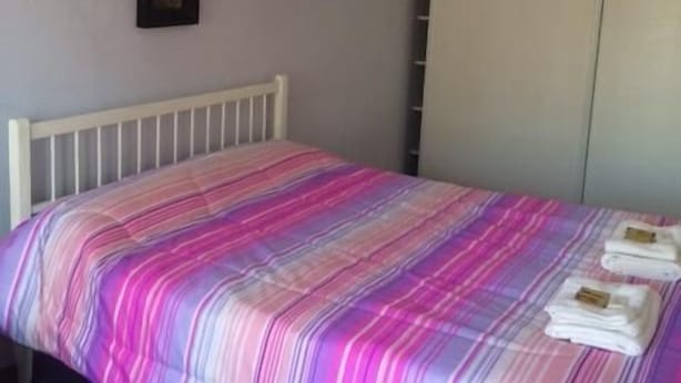 A bedroom with a bed, a white headboard, a wardrobe, and two framed pictures on the wall. - Pindo Guazu Hostel (Buenos Aires)