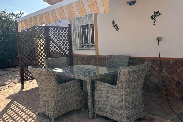 Une terrasse extérieure avec une table à plateau de verre et des chaises en osier.