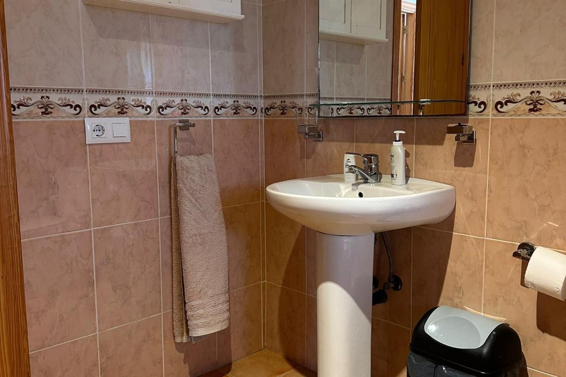 A bathroom with a white sink, a towel hanging on the wall, and a toilet paper holder.