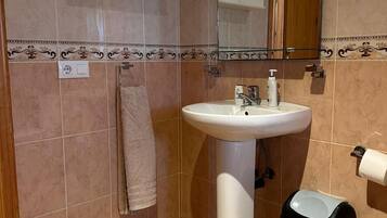 A bathroom with a white sink, a towel hanging on the wall, and a toilet paper holder.