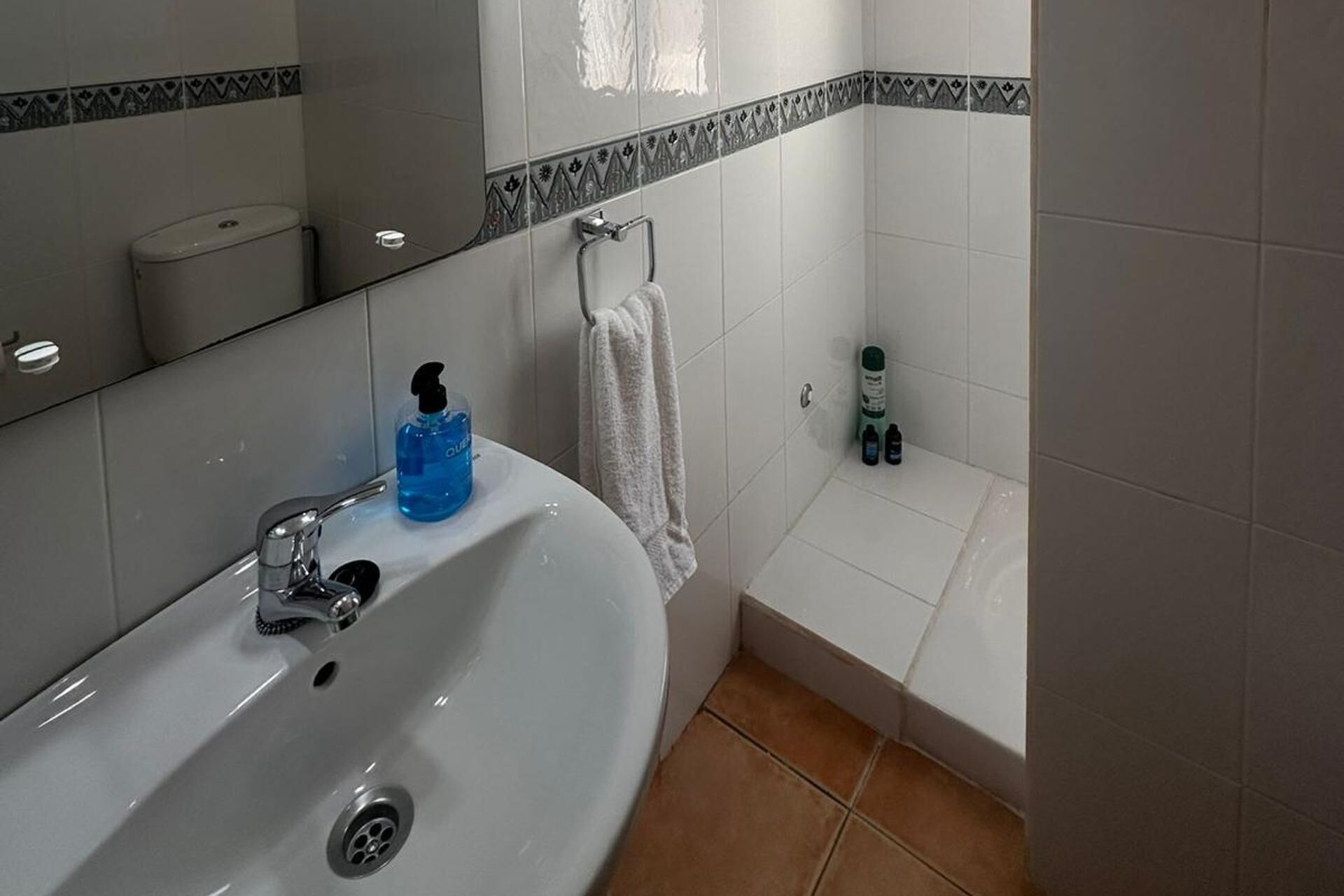 A bathroom with a white sink, a mirror, a towel hanging on the wall, and toiletries on the floor.