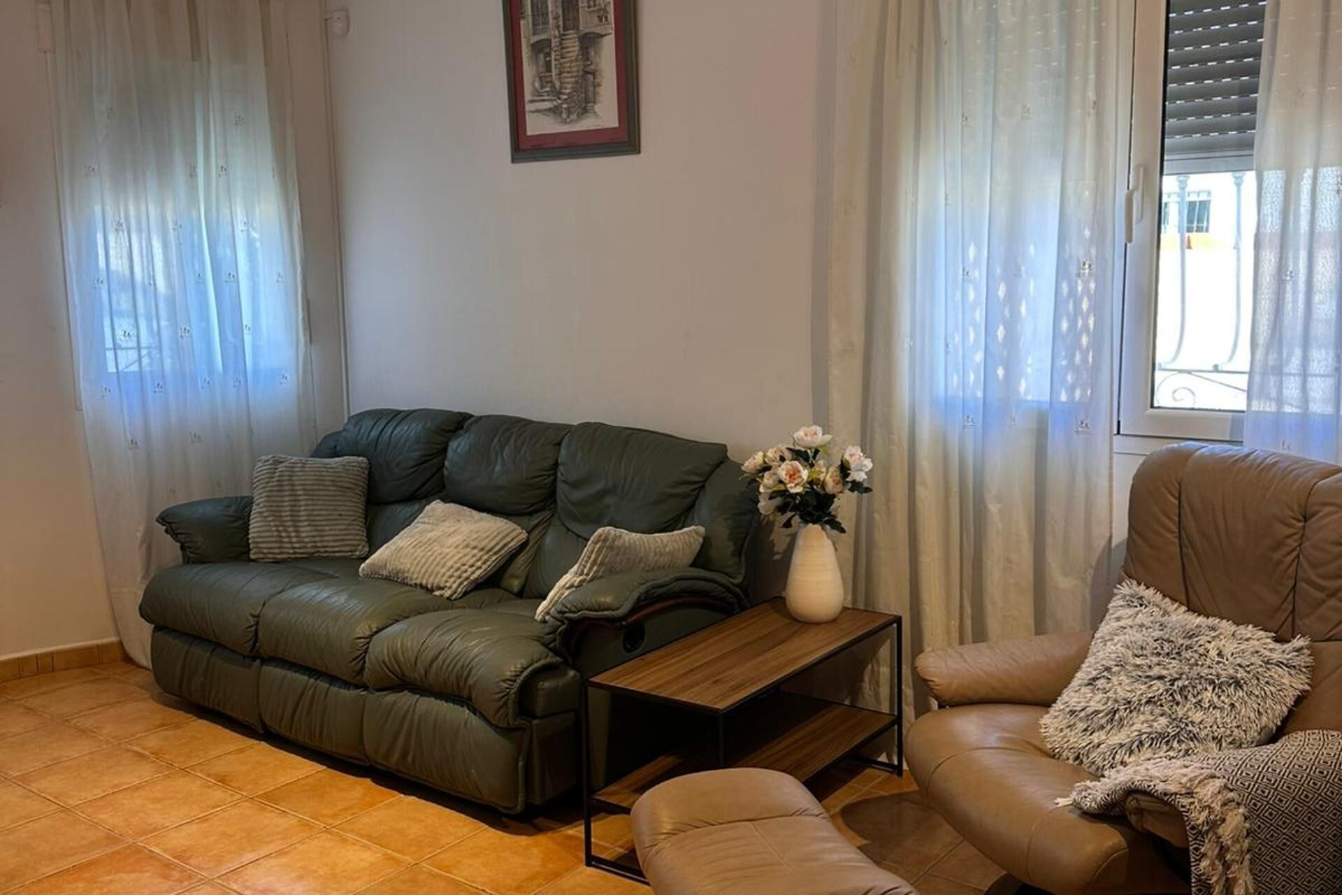 A living room with a green leather sofa, a brown leather armchair, a small wooden coffee table, and a vase with flowers.
