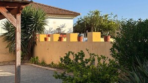En byggnad med ett tak täckt av takpannor, en beige vägg med planterade blommor och en pergola av trä.