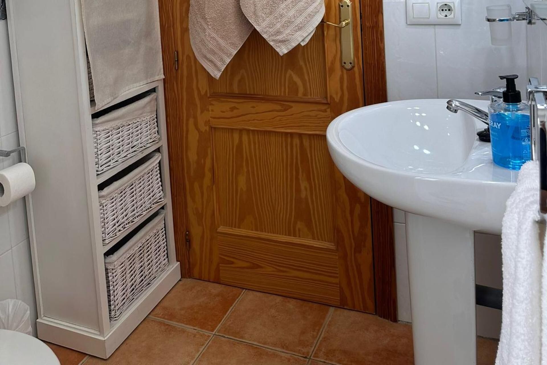 A bathroom with a wooden door, a white sink with a blue bottle, and a toilet.