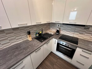 Een moderne keuken met witte kasten, een zwarte spoelbak, een ingebouwde oven en een koffiezetapparaat.