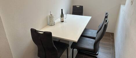 A small dining area with a white table, two black chairs, a wine bottle, and a candle holder.