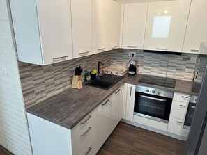 Een moderne keuken met witte kasten, een donker aanrecht, een inbouwoven en een koffiezetapparaat.