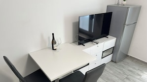 Une petite cuisine équipée avec un plan de travail blanc, une télévision, un réfrigérateur et deux chaises.