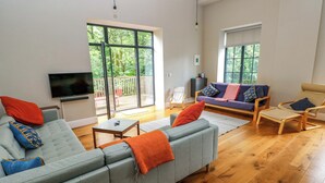 A modern living room with a grey sofa, a wooden coffee table, and a beige armchair. There is a large window with a view of greenery outside. - The Old Creamery (Llandeilo)