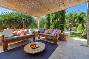 An outdoor seating area with two wooden sofas, a round wooden table with drinks, and a thatched roof overhead. - Villa 'Llenaire' with Mountain View, Wi-Fi and Air Conditioning (Illes Balears)