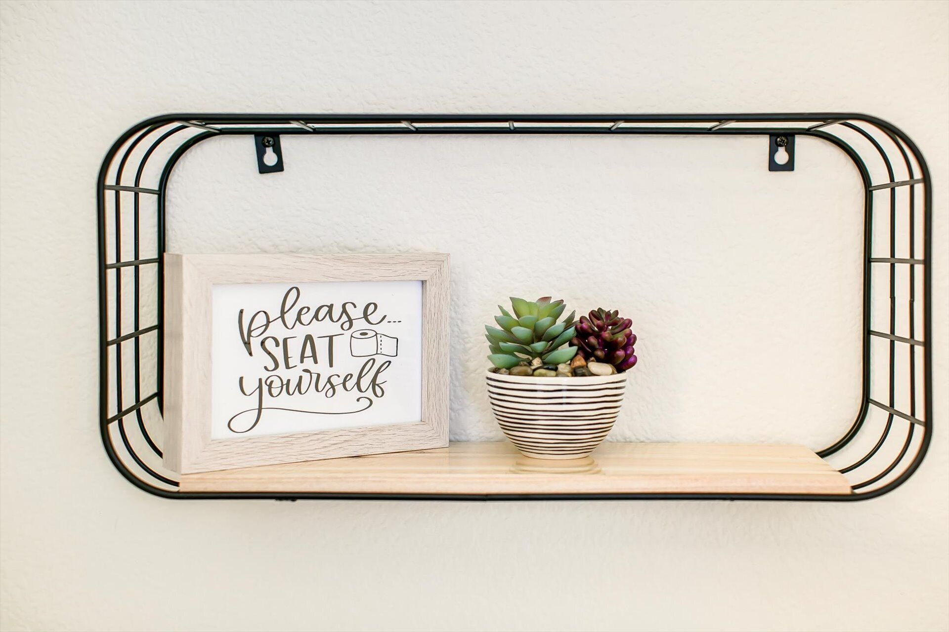 A wall-mounted shelf with a framed sign saying "please... SEAT yourself" and a potted succulent plant.