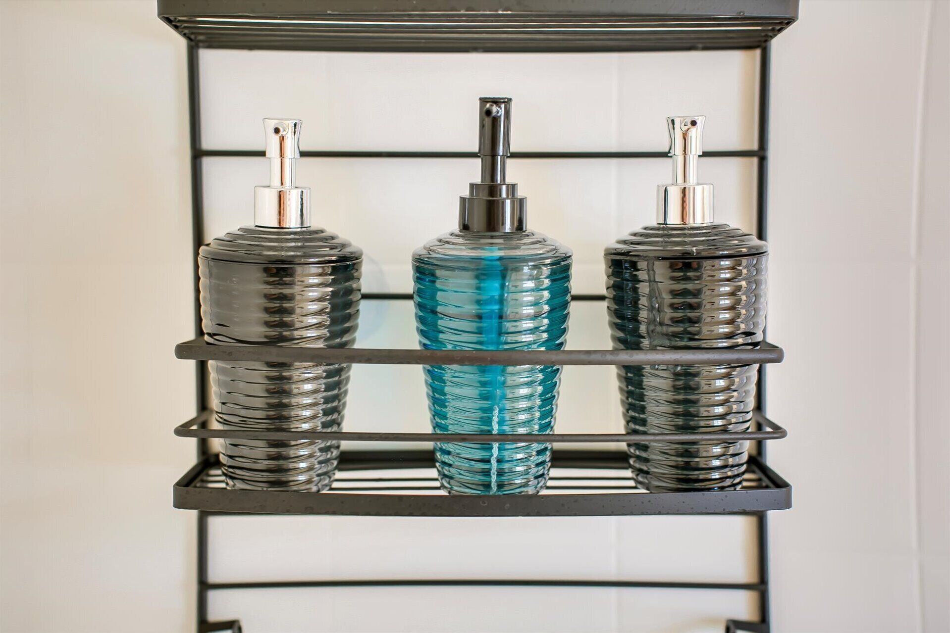 A metal shelf with three glass bottles, two with metallic caps and one with a blue cap.