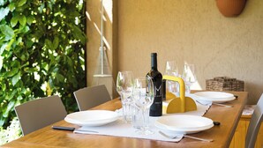 Una mesa de comedor dispuesta con platos, vasos y una botella de vino, rodeada de sillas y una planta en maceta.