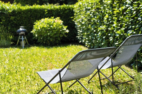 A grassy outdoor area with two mesh chairs and a barbecue grill.