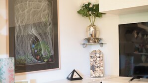 Un dibujo de tiza enmarcado, un jarrón con flores, un reloj y un televisor sobre una pared blanca.