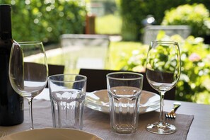 Ein Tisch, gedeckt mit Weingläsern und einer Flasche, draußen vor einer grünen Kulisse.